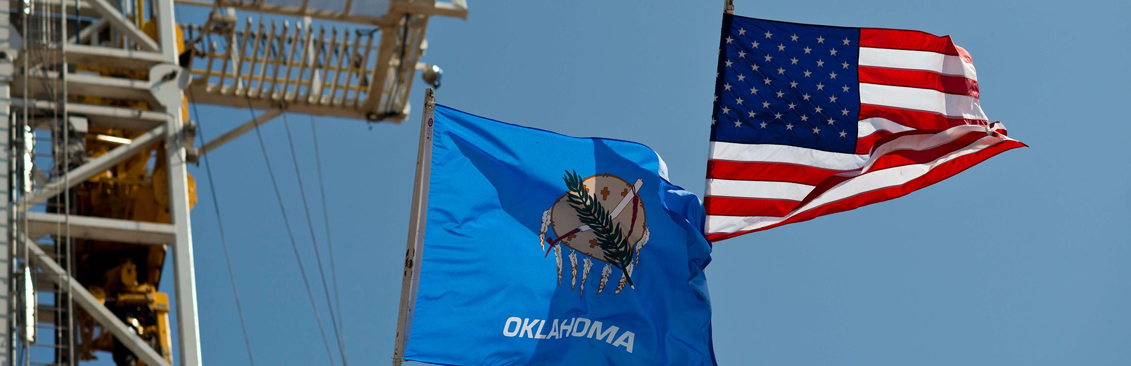 United States and Oklahoma flags waving near oil rigging